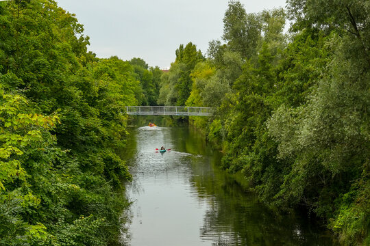 Kayaking on the Karl Heine Canal in Leipzig. Several kayaks can be seen on the water. The canal is lined with lush vegetation and spanned by a bridge.