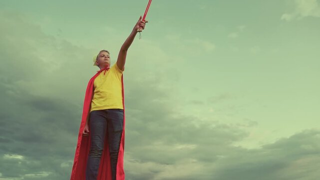 teenage boy plays knight against background sky. concept children play. childhood dream superhero. defend himself with sword crown his head. superman winner. fantasy childhood dream. red cape wind