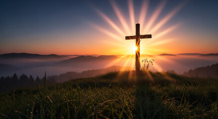 A wooden Christian cross stands silhouetted on a grassy hilltop against a vibrant sunrise, with sun rays emanating from behind it and a misty landscape in the background.