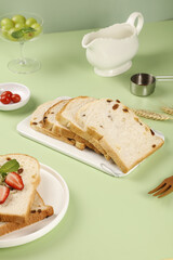 Sliced Handmade Raisin Bread with Fresh Fruit on Green Background - Bright Kitchen Scene