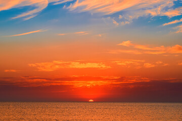 The sun sinks into the sea surrounded by clouds, late evening over a warm sea, the splendor of autumn sunsets during the period of soft and warm velvet autumn