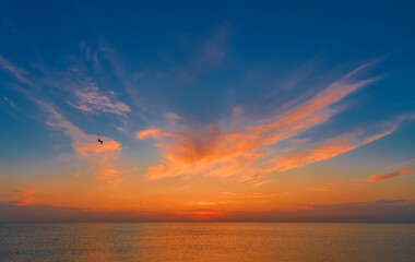 Fantastic sunset over sea, bright colors of autumn sky over the calm sea, a seagull soars over water, an idea for a poster about velvet season at sea as period of mild and warm weather before winter