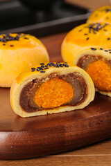Traditional Chinese mooncakes with egg yolk filling and black sesame seeds on wooden board