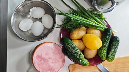 Set of fresh ingredients including cucumbers, eggs, potatoes, ham and herbs prepared for cooking