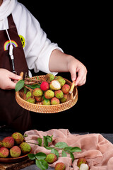 Freshly Picked Hainan Litchi Fruits in Wicker Basket with Green Leaves on Black Background