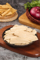Dried bean curd skin sections and handmade tofu sheets on wooden board with fresh vegetables