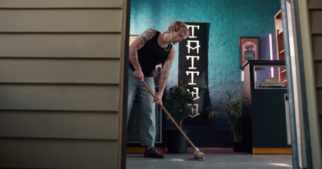 Tattoo studio, man and sweeping floor for cleaning, hygiene and housekeeping with artist. Shop, person and broom for chores, remove dust and dirt for maintenance with professional in small business