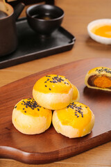 Handmade egg custard dessert pastries with black sesame seeds on wooden serving board