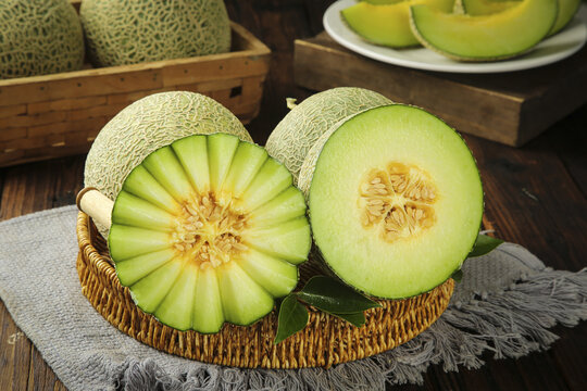 Fresh Hainan Melons Cut in Half Showing Green Flesh in Wicker Basket on Wooden Table
