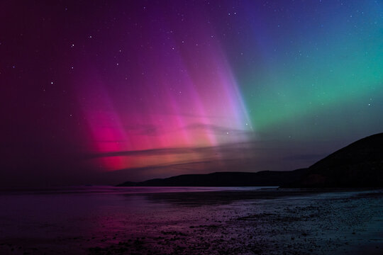 Vibrant northern lights over a dark coastal landscape at night