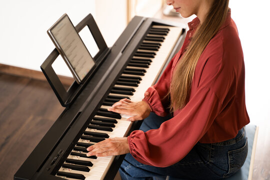 Top view of woman playing on an electronic piano indoors in daylight, using tablet with exercises, distance learning for musicians to play classical digital piano, modern lifestyle - Powered by Adobe