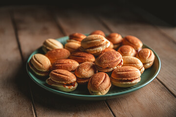 Plate full of delicious homemade nut shaped cookies filled with boiled condensed milk resting on a wooden table, creating a cozy and tempting scene