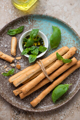 Middle close-up of salted breadsticks grissini served with basil oil on a brown plate, vertical shot, elevated view