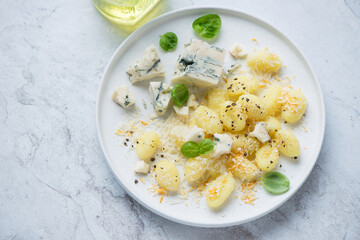 Plate of potato gnocchi with blue cheese and basil, horizontal shot on a white stone background, elevated view