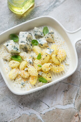 Beige serving tray with italian potato gnocchi and blue cheese, vertical shot on a grey granite background, elevated view