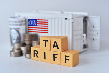 Carton printed word "Tariff"  beside coins and US dolla bills with container. US new import taxes announced by Donal Trump. Affected to baseline tariff, reciprocal tariffs,consumers,global economy