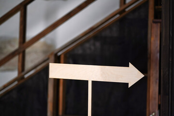 Fototapeta premium Wooden directional arrow sign indoors on blurred rustic background with stairs