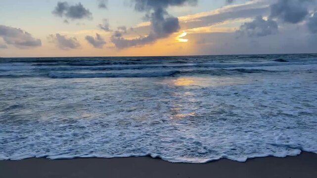 Golden sunset over ocean waves with glowing reflections on sandy beach horizon