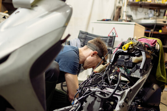 Skilled mechanic diligently repairing a scooter engine in a workshop, focusing on complex wiring and components. Captures vehicle maintenance and professional service in a garage environment.