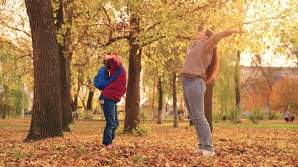 mother and little child in an autumn park throw dry leaves up, happy family, live fun with mom, cheerful kid plays with foliage and parent hands throwing leaf fall, parental care of girl, nature walk.