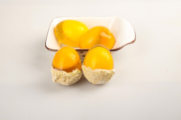 Fresh egg yolks in bowl with breaded hard-boiled egg halves on white background