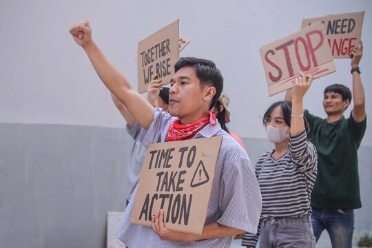Young Asian Man With Red Bandana Raising Fist While Calling For Immediate Action And Change - Powered by Adobe