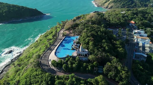 Aerial tilt-up push-back reveal over Promthep Cape&rsquo;s blue plaza to rocky headland, Phuket