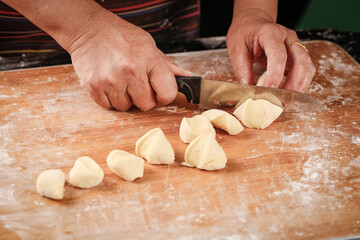 Baker cutting fresh wheat dough portions on wooden board with knife - homemade bread making process