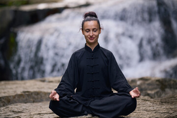 A woman sits in lotus pose, practicing yoga and tai chi under a tropical waterfall, meditating with calm strength and mindfulness, fully connected to the energy of nature, tranquility and inner