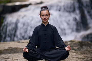 A woman sits in lotus pose, practicing yoga and tai chi under a tropical waterfall, meditating with calm strength and mindfulness, fully connected to the energy of nature, tranquility and inner
