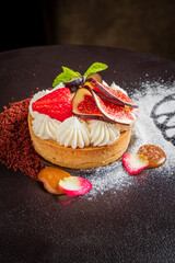 A gourmet tart topped with fresh strawberries and figs, elegantly garnished