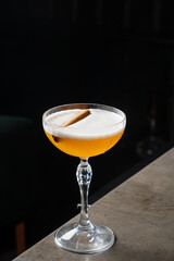 A crafted cocktail showcases a frothy top, complemented by a cinnamon stick, on a chic bar surface