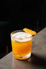 A vibrant cocktail with a glossy finish, enriched by an orange slice, rests on a sleek bar surface