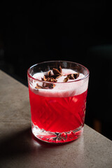 Bright red drink garnished with spices sits atop a sleek bar surface in low light