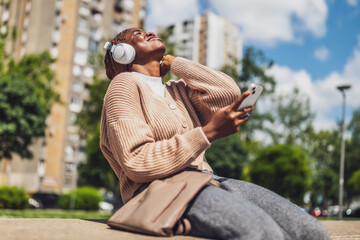 Portrait of a cheerful black woman in her 20s using her mobile phone outdoors in an urban setting,...