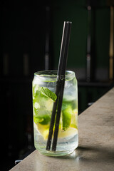A clear drink with mint leaves and citrus is placed on the bar, inviting refreshment