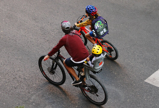 Vuelta al cole en bicicleta de ni&ntilde;os y padre con casco y mochila por la carretera