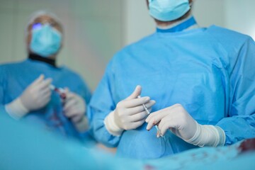 Two surgeons wearing medical scrubs, masks, and gloves stand ready during a medical procedure. One holds a syringe as they prepare to help a patient inside Hospital Santa Maria