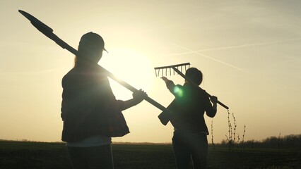 Farmer girls walk across the field to work with a shovel and rake at sunset in the sky, young and...