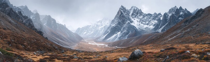 Panoramic view rugged mountain valley under overcast sky, golden autumn vegetation, and snow-capped peaks. Landscape