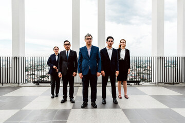 Diverse business team in formal attire standing on a modern rooftop terrace with city skyline views, confident leadership concept in urban corporate setting.