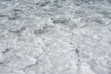 Sea foam on the pebble beach after breaking wave. Rough sea.