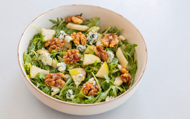 fresh fall salad in a bowl with arugula, ripe pear slices and crunchy walnuts, healthy autumn lunch idea with vibrant colors