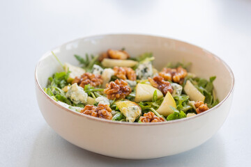 fresh fall salad in a bowl with arugula, ripe pear slices and crunchy walnuts, healthy autumn lunch idea with vibrant colors