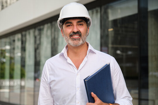 Confident architect or investor in white helmet outdoors holding folder
