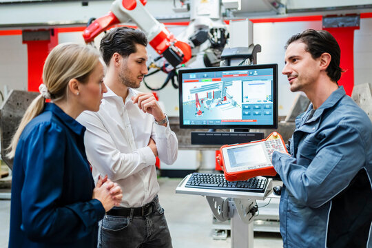Engineer explaining controller device to colleagues in meeting at robot factory