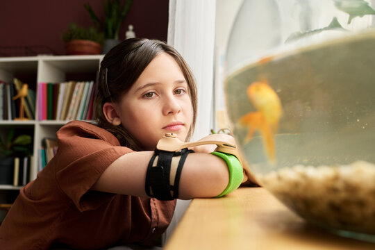 Girl with prosthesis contemplating goldfish at home