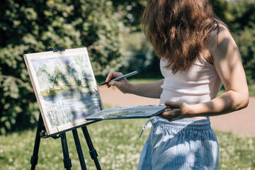 Artist painting landscape on easel outdoors in park