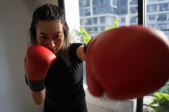 Focused young female boxer training indoors with red gloves in urban setting during late afternoon light