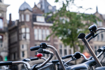 Obraz premium Close-up of bicycle handlebars and bells in a European city setting, with blurred historic architecture in the background, capturing the urban cycling culture and charm of European streets.